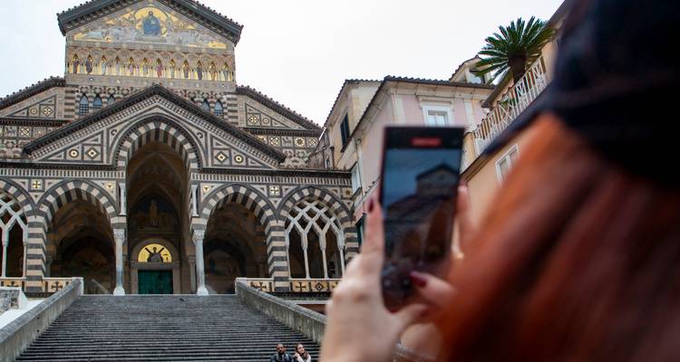 Visitor capturing a photo of the ornate striped façade of Amalfi Cathedral while standing on the staircase.