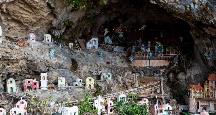 Miniature village nativity scene set inside a rocky grotto, decorated with tiny houses and figurines.