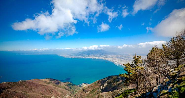 Expansive aerial view of the Bay of Naples with distant cityscape under a bright blue sky.