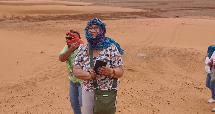 Zwei Frauen in Schals gehüllt stehen auf sandigem Gelände und machen Fotos im Wind