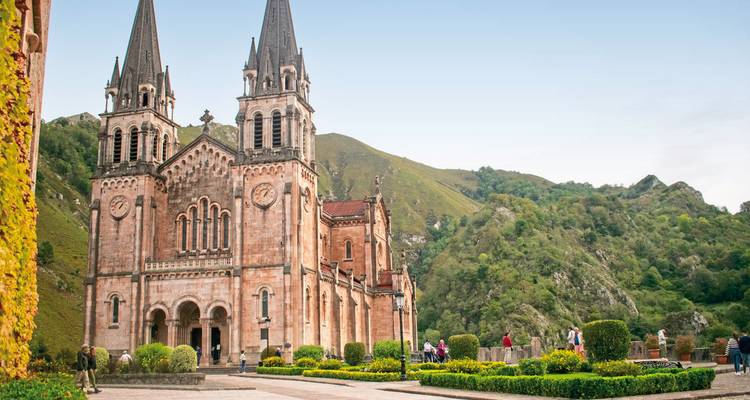 Basilique historique avec des montagnes en arrière-plan, des gens se promènent.