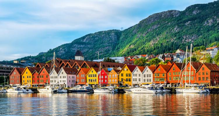 Colorful houses and boats along a waterfront with a mountainous backdrop.