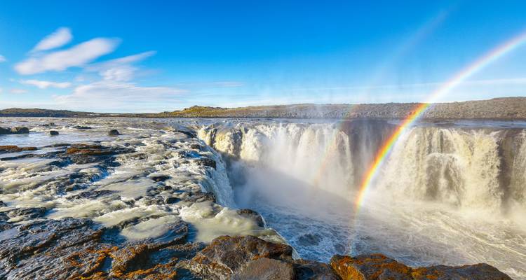 Cascade puissante avec un arc-en-ciel et un terrain rocheux.