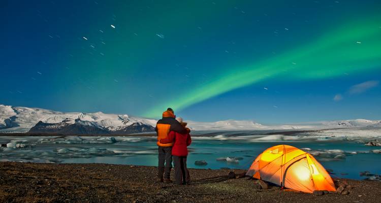 Des gens regardant les aurores boréales au-dessus d'un paysage gelé, avec une tente.