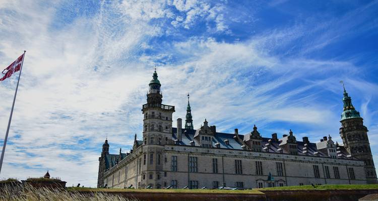 Historical castle with a cloudy sky and Danish flag.