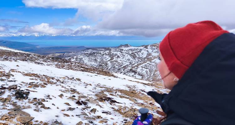 Person in winter clothing overlooking snowy mountains.