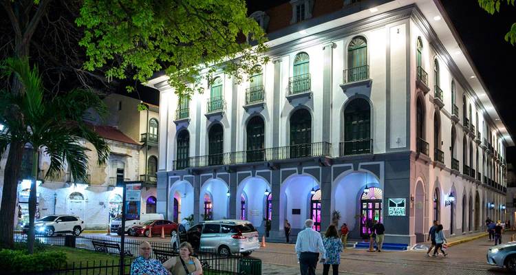Vue nocturne d'une rue avec des bâtiments illuminés et des gens qui marchent.