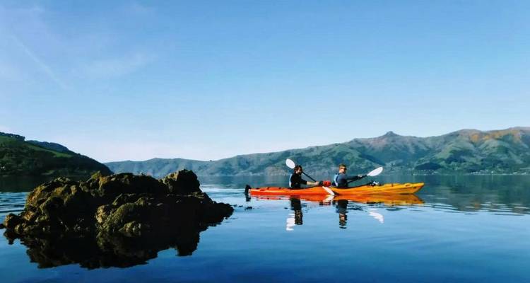 Dos kayakistas en un lago tranquilo con montañas al fondo.