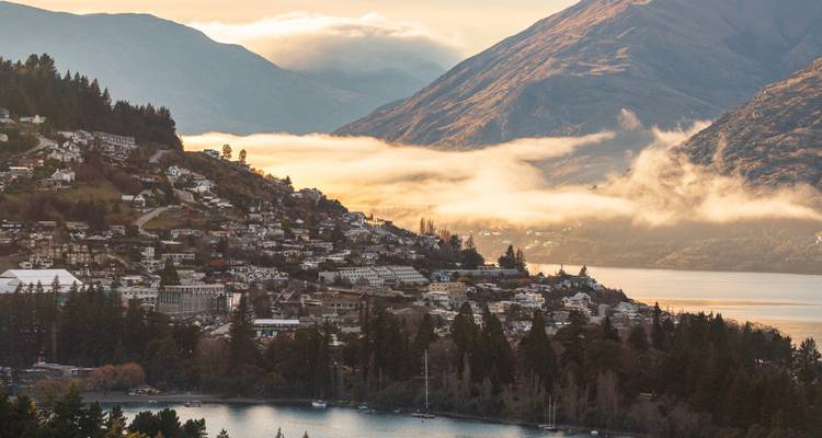 Maisons sur une colline surplombant un lac avec des montagnes et des nuages.