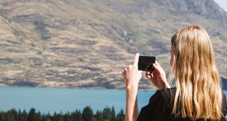 Femme prenant une photo d'un paysage de lac et de montagne.