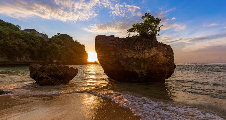 Sunset on a beach with rocky formations and waves.