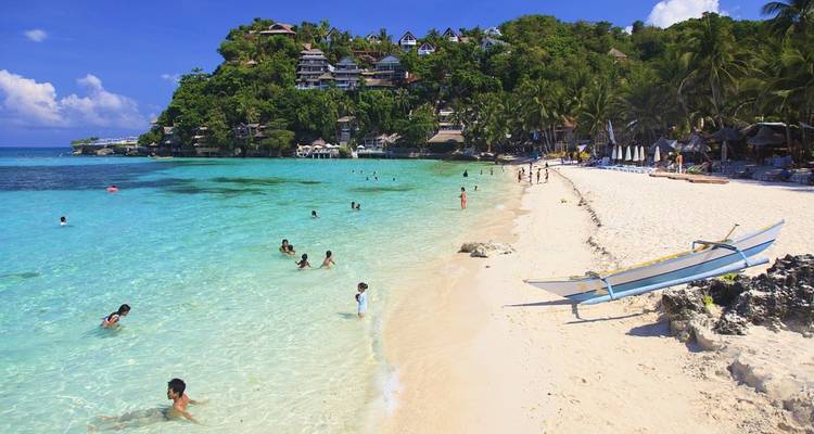 People swimming at a sandy beach with clear blue water.