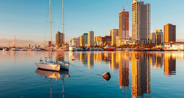 Yachts in a city harbor at sunset with a modern skyline.