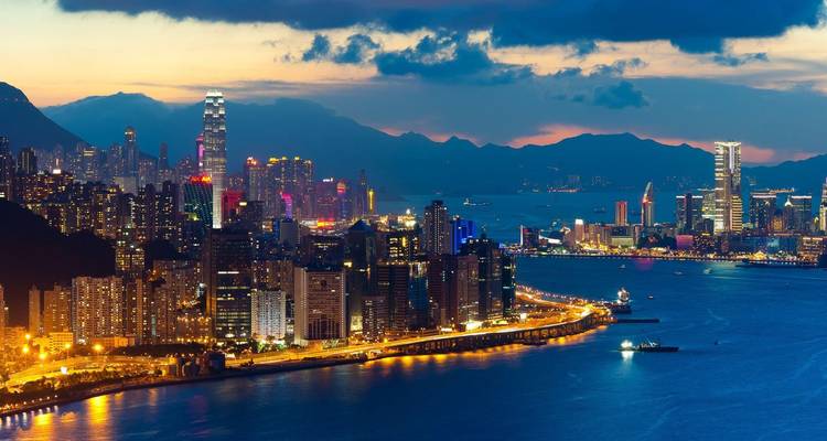 Cityscape of Hong Kong at dusk with lit up skyscrapers along the river.