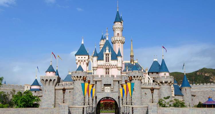 A view of a castle with towers and colorful flags in a theme park.