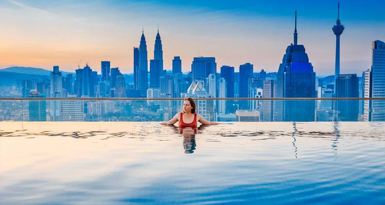Une femme dans une piscine à débordement donnant sur un horizon urbain avec des gratte-ciel.