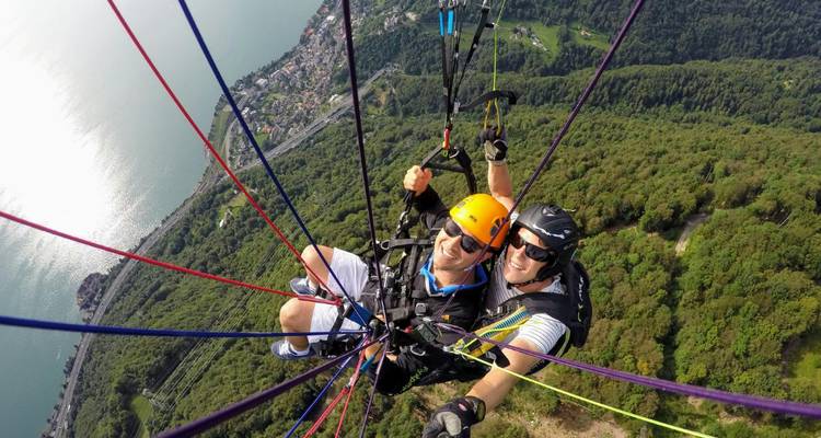 Two people tandem paragliding over a landscape.