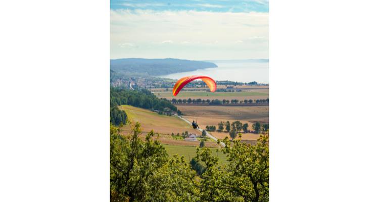 A paraglider soaring above a scenic landscape with a lake.