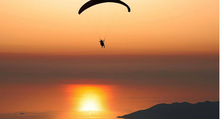 Paraglider silhouetted against a beautiful sunset over water.