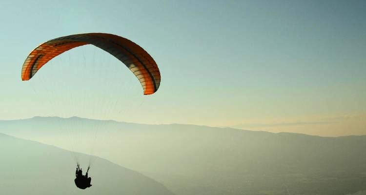 Solitary paraglider against a mountainous backdrop.