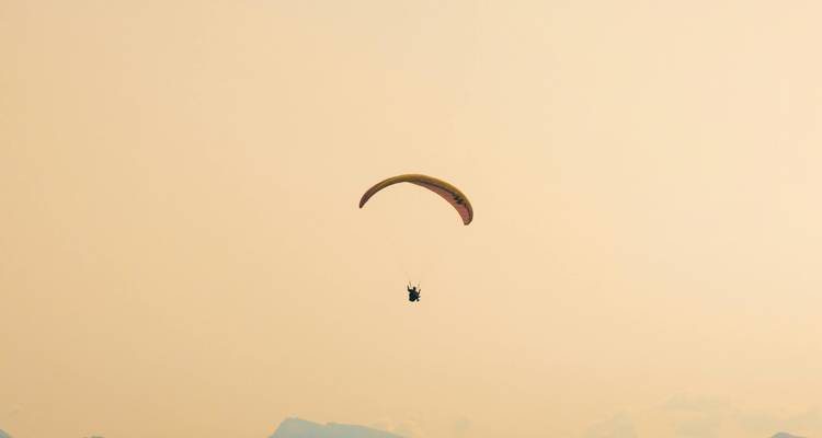 Paraglider flying in a hazy sky with mountains visible.