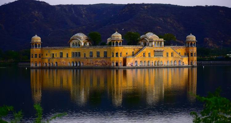 Palais Jal Mahal partiellement submergé dans un lac avec des collines en arrière-plan.