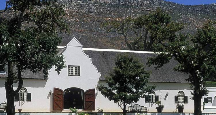 Ein traditionelles Gebäude im Kap-Holländischen Stil vor einer zerklüfteten Bergkulisse.