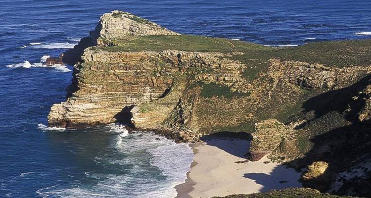 Klippenblick aufs Meer mit Wellen, die auf schroffe Felsen krachen und einem Sandstrand darunter.