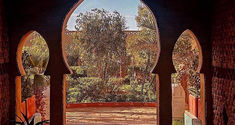 Vue sur la cour à travers une arcade marocaine, jardin luxuriant visible.