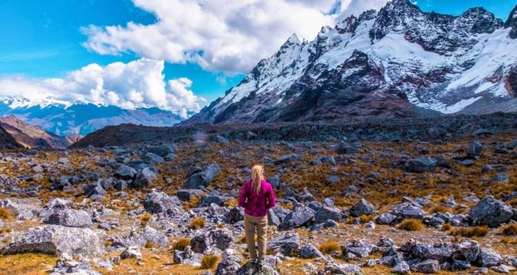Persona de pie sobre terreno rocoso, contemplando montañas nevadas.
