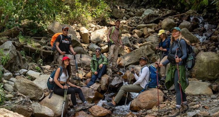 Grupo de senderismo posando, sentado junto a un pequeño arroyo sobre rocas.