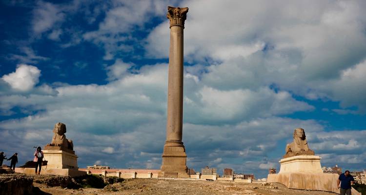 Zwei Sphinxstatuen und eine Säule unter einem blauen Himmel.