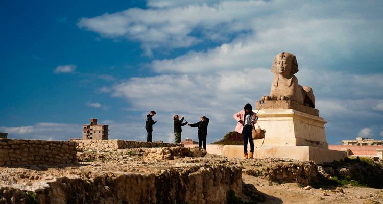 Menschen, die in der Nähe einer Sphinx-Statue auf Ruinen Fotos machen.