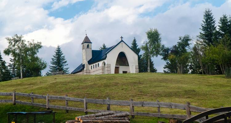 Une petite église sur une colline herbeuse entourée d'arbres.