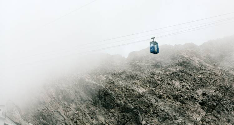 Seilbahn, die in einen felsigen, nebelbedeckten Berg hinaufführt.