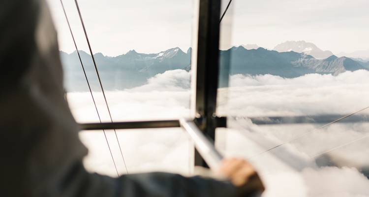 Blick aus einer Seilbahn mit Berglandschaft und Wolken.