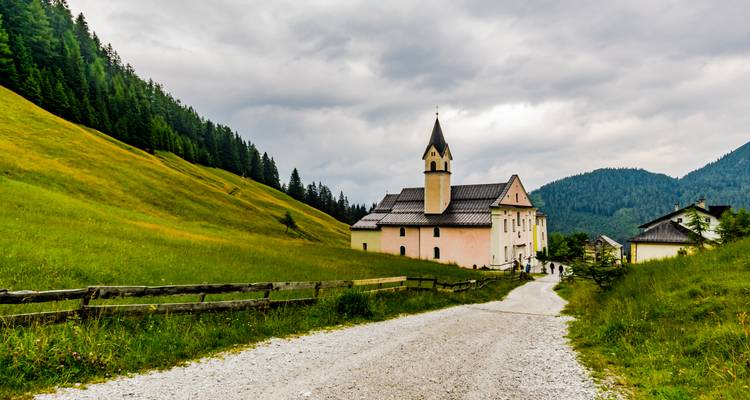 Église pittoresque dans une vallée montagneuse avec des gens sur un sentier.