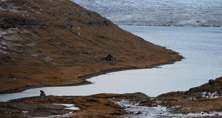 Remote cabin by a lake surrounded by brown hills.