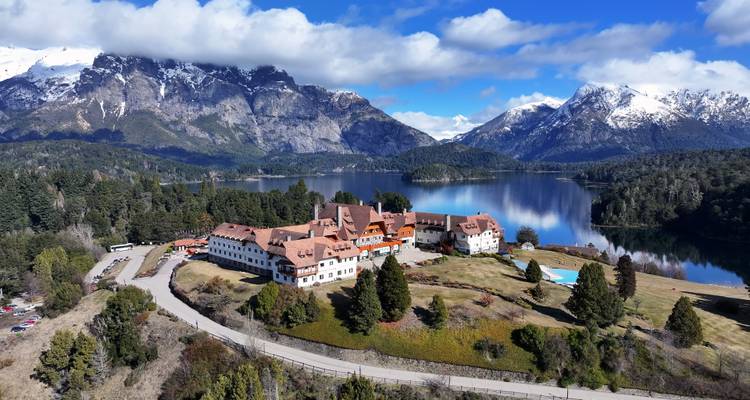 Vue au bord du lac avec un grand bâtiment et des montagnes en arrière-plan.