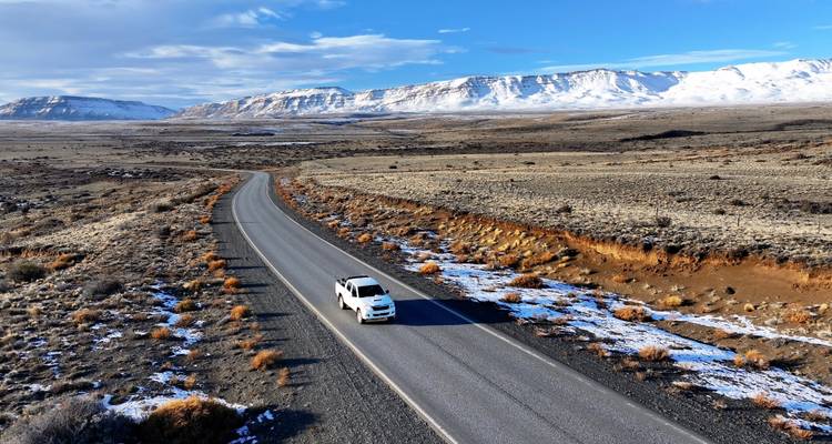 Voiture roulant sur une route à travers un paysage montagneux avec de la neige.