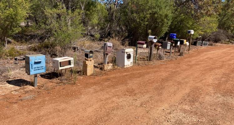 A row of unique and colorful mailboxes along a dirt road.