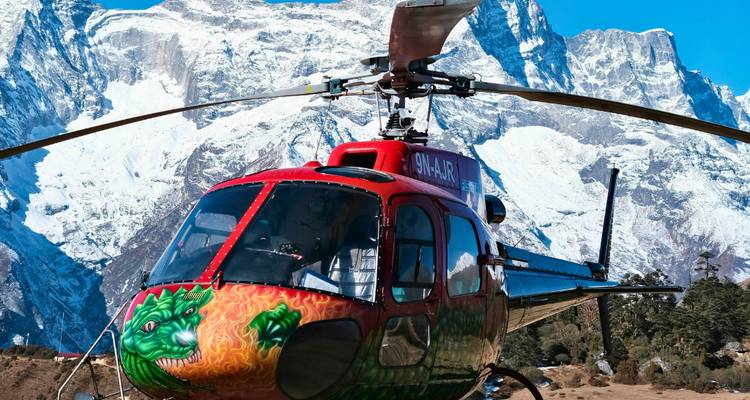 Helicopter with a painted dragon design next to snow-covered mountains.