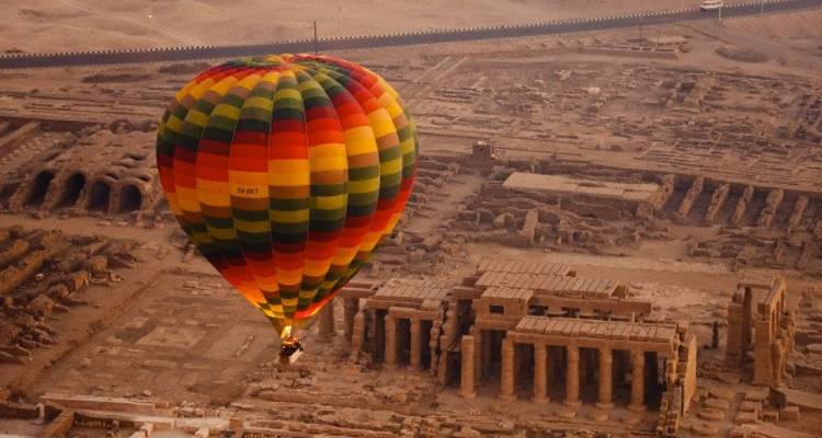 Montgolfière au-dessus de ruines antiques dans un paysage désertique.