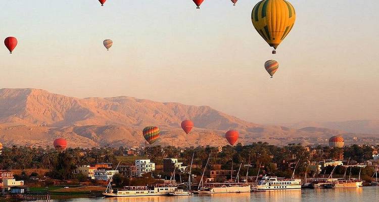 Montgolfières au-dessus d'une rivière avec des montagnes et des bâtiments.