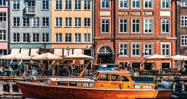 Colorful facades and open-air cafes along a lively waterfront with wooden pleasure boat in foreground.