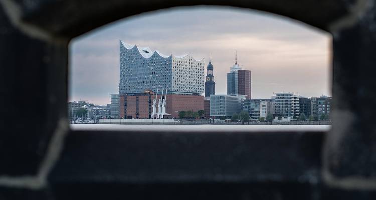 Framed view of the futuristic glass concert hall on Hamburg's waterfront through a stone opening.