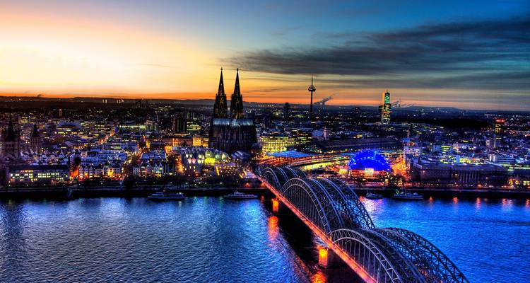 Vibrant twilight aerial of Cologne with illuminated bridge, cathedral and city skyline beside the Rhine.