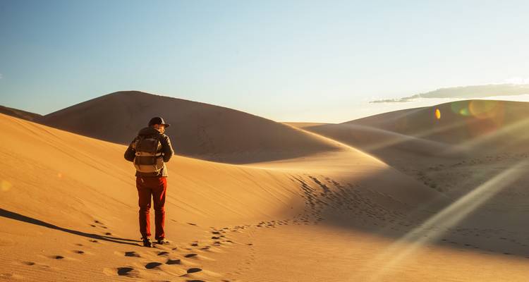 Person mit Rucksack, die durch Wüstendünen wandert.