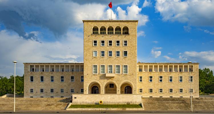 Gran edificio de piedra con una bandera en la parte superior bajo un cielo azul.