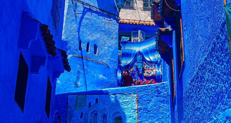 Ruelle bleu vif à Chefchaouen ornée de textiles et d'art mural baignée de soleil.